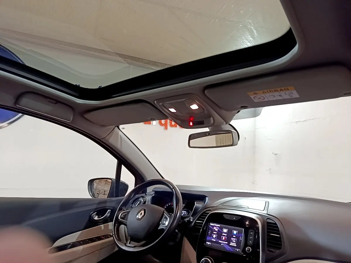 Vue intérieure côté conducteur du Renault Captur Intens 2019, volant cuir, toit panoramique et écran tactile allumé.