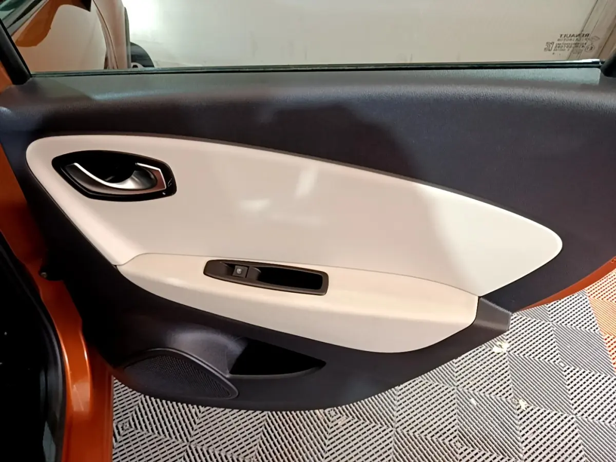 Porte intérieure côté gauche beige et noire du Renault Captur orange 2019, avec poignée et commande de vitre électrique.