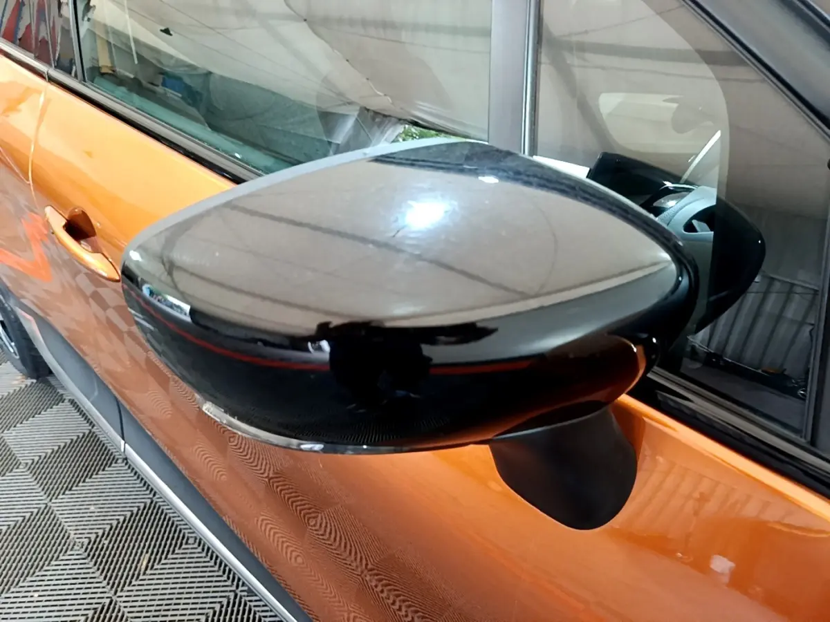 Rétroviseur noir en gros plan côté gauche sur Renault Captur orange, avec reflet intérieur visible.