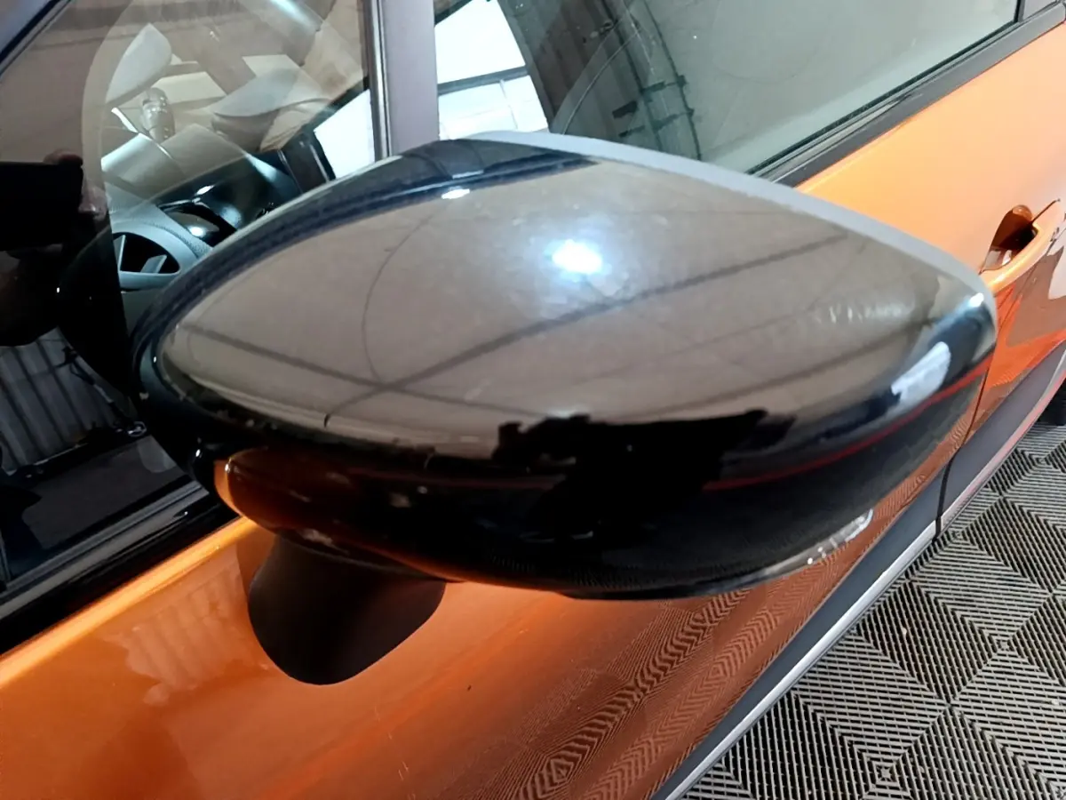 Rétroviseur latéral gauche noir brillant sur Renault Captur orange vu de près côté conducteur.