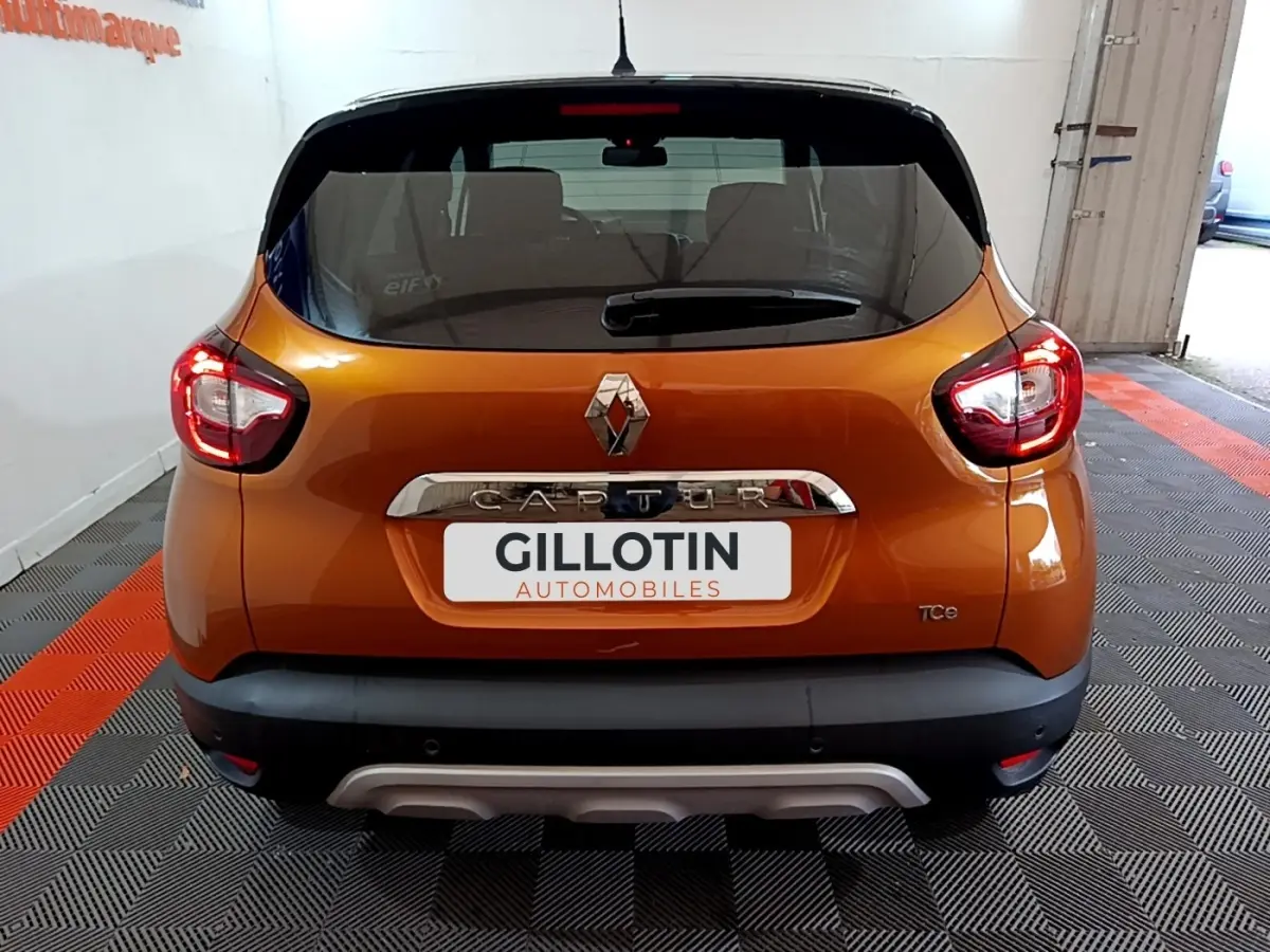 Vue arrière d'un Renault Captur orange avec feux allumés et logo chromé sur fond noir.