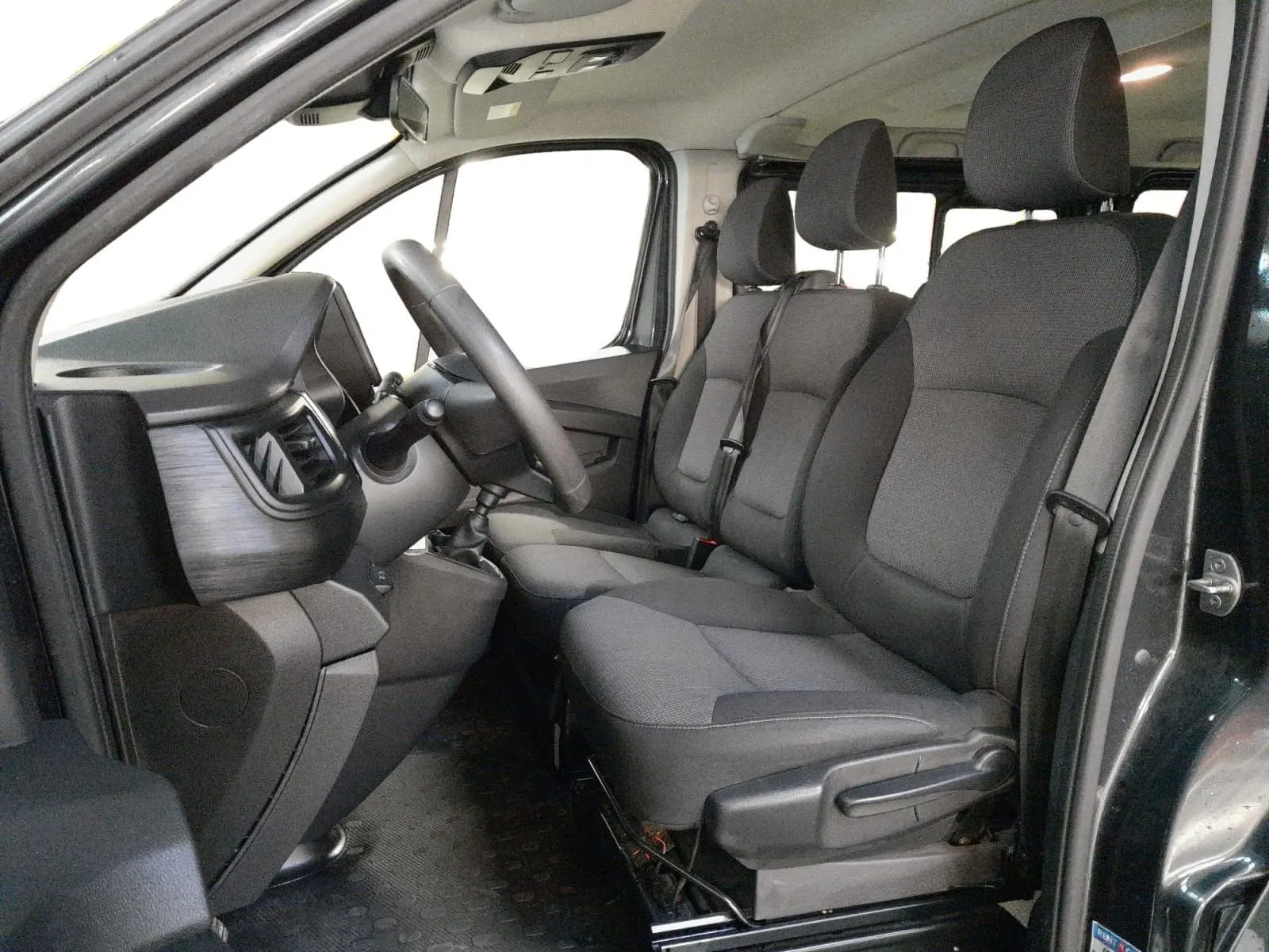 Vue intérieure côté conducteur du Renault Trafic Combi gris comète, montrant les sièges avant et le tableau de bord.