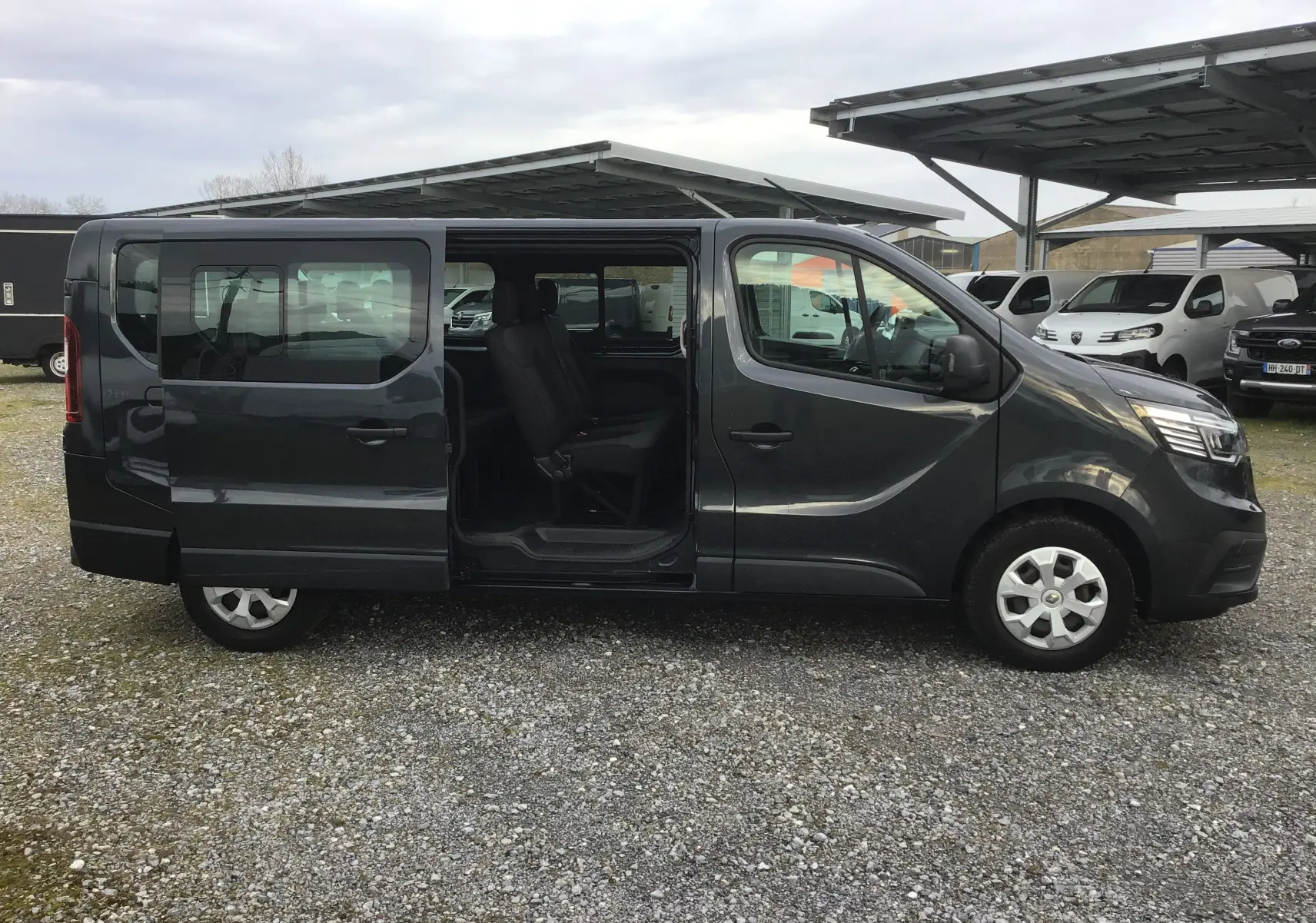 Vue latérale gauche d’un Renault Trafic Combi gris comète 2022 avec porte coulissante ouverte montrant l’intérieur 9 places.