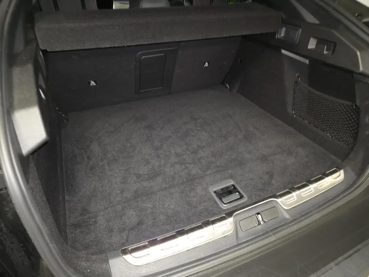 Coffre ouvert vu de l'arrière d'une Peugeot 408 noire, avec tapis de sol noir et filet de rangement latéral.