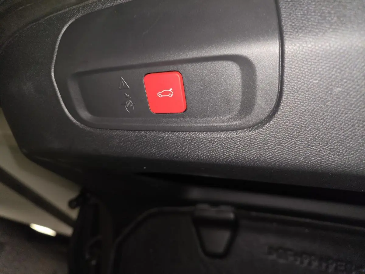 Bouton rouge d'ouverture du coffre sur panneau intérieur noir d'une Peugeot 408 2024 hybride rechargeable.