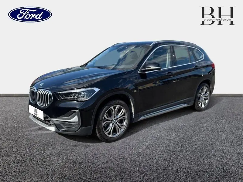 BMW X1 xDrive25e saphirschwarz vue 3/4 avant droit, avec jantes alliage et calandre chromée distinctive.