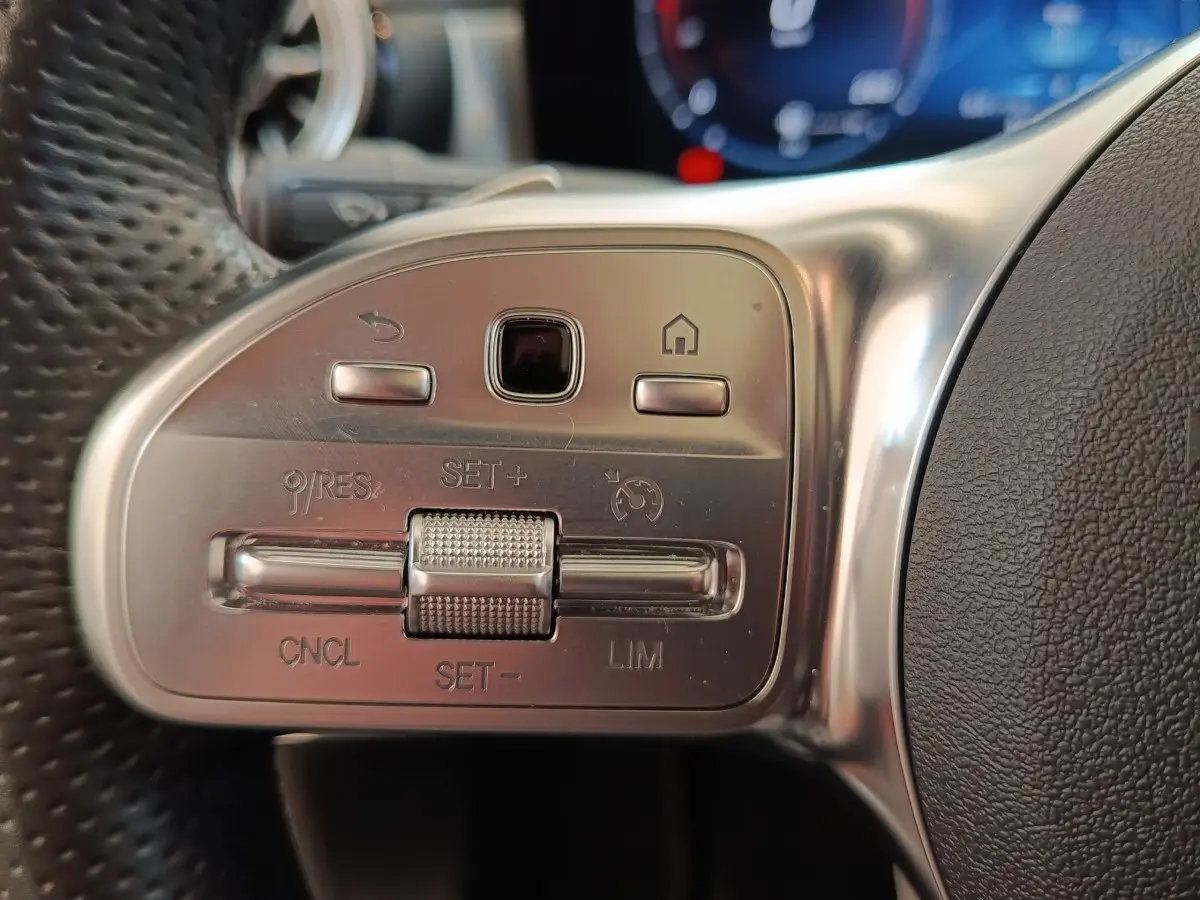 Gros plan sur les commandes en aluminium et cuir du volant multifonctions de la Mercedes Classe A blanche, côté gauche.