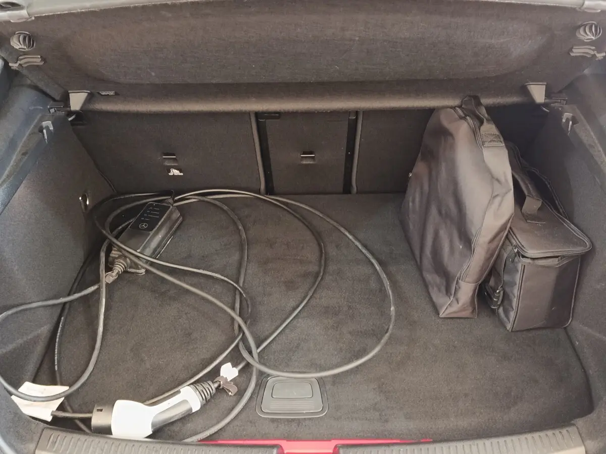 Coffre ouvert d’une Mercedes Classe A 250 e AMG Line blanc, avec câble de recharge et sac de rangement.