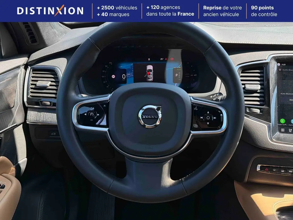 Vue intérieure centrée sur le volant cuir noir et le tableau de bord digital du Volvo XC90 hybride 2024.