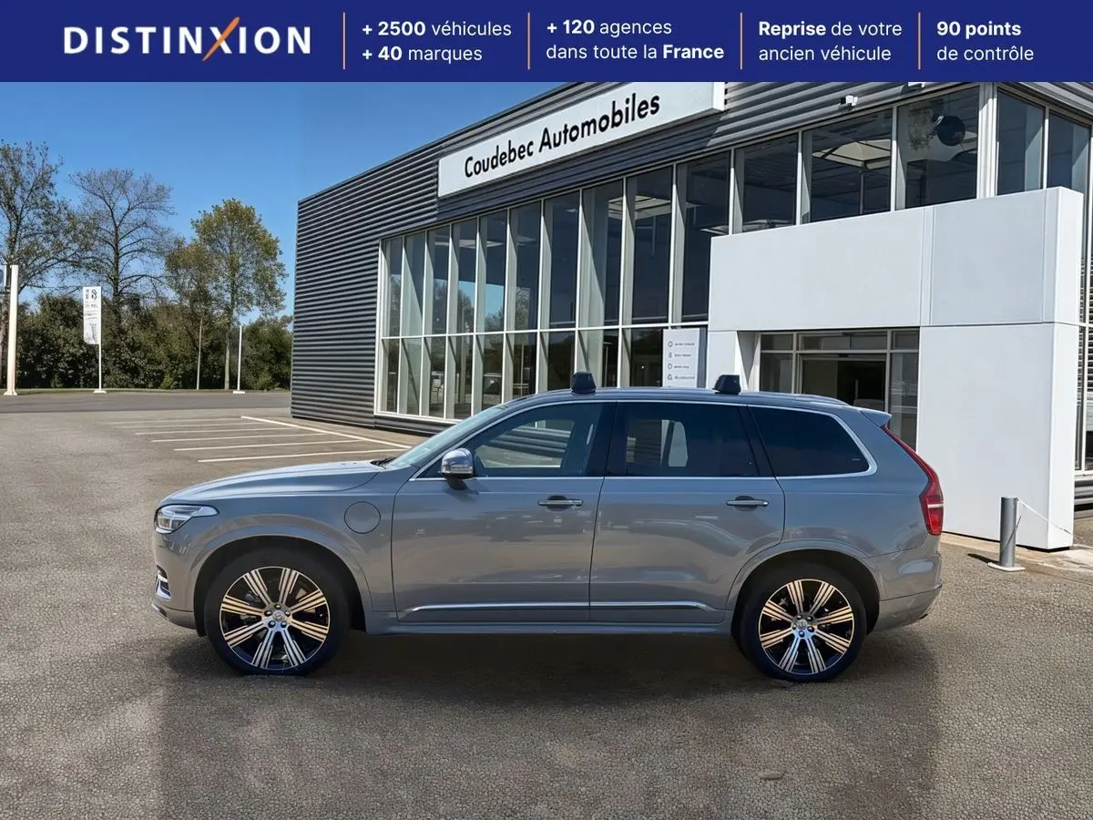 Vue de profil côté gauche d'un Volvo XC90 gris 2024 hybride rechargeable avec jantes alliage et barres de toit.