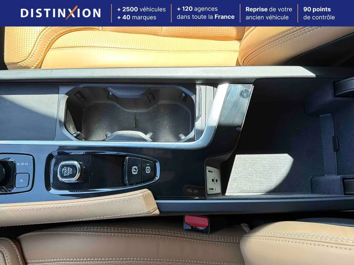Vue plongeante sur la console centrale cuir beige du Volvo XC90 gris avec bouton démarrage et porte-gobelets.