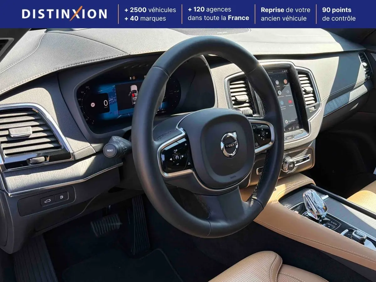 Vue intérieure du tableau de bord et volant noir du Volvo XC90 2024 avec écran tactile vertical et sellerie cuir beige.