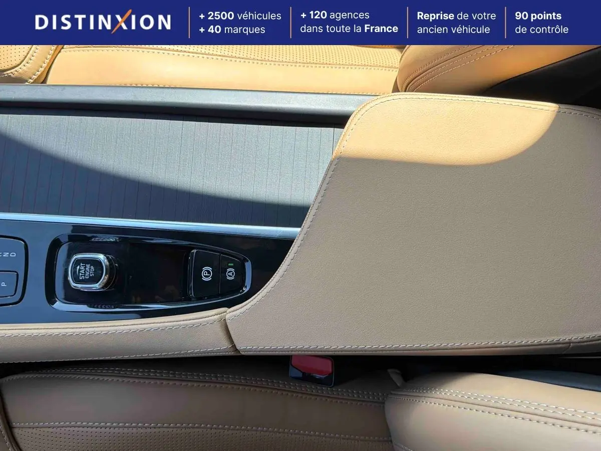 Gros plan sur la console centrale beige du Volvo XC90 2024 avec bouton start/stop et commandes de frein à main.