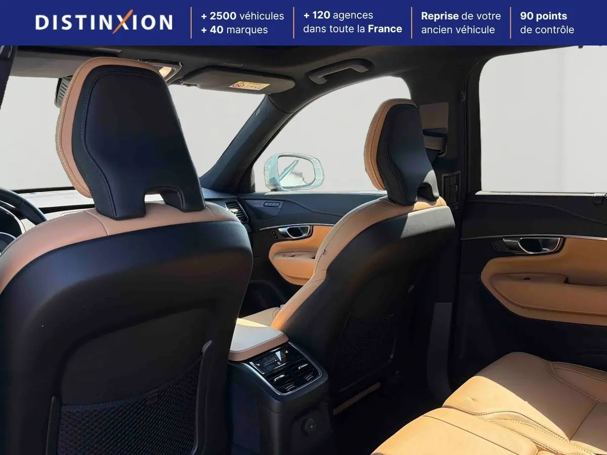 Vue intérieure arrière du Volvo XC90 2024 montrant les sièges en cuir bicolore beige et noir avec console centrale et toit ouvrant panoramique.