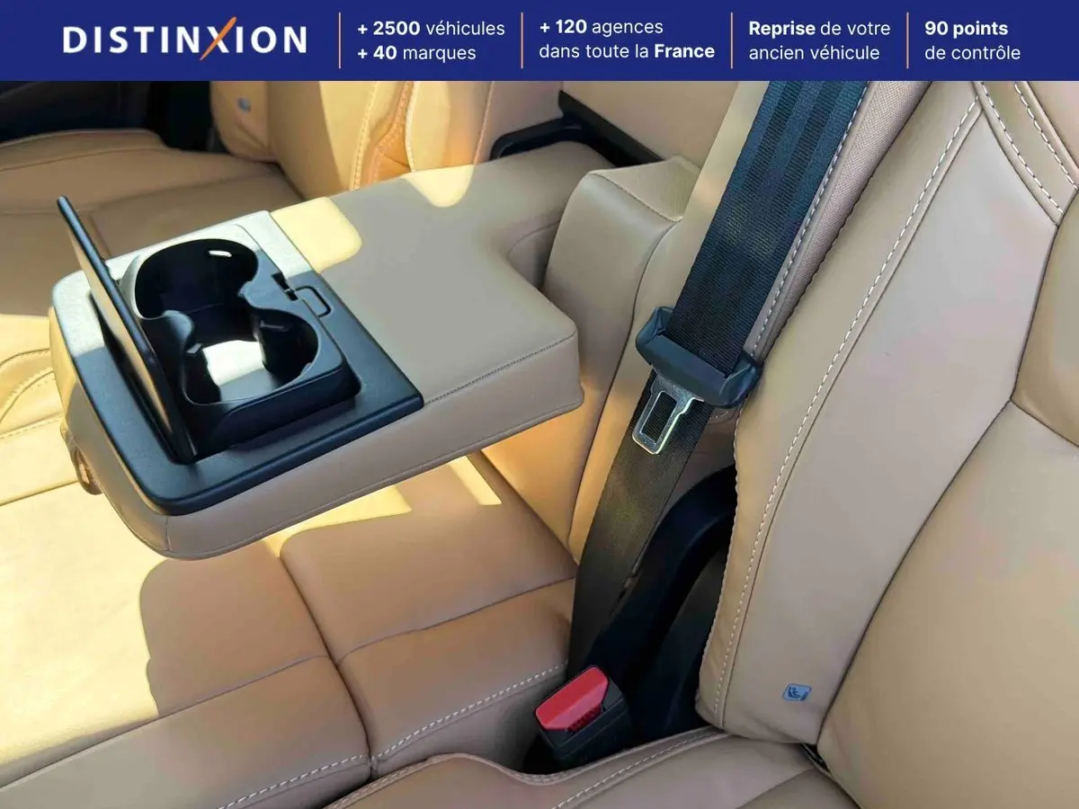 Détail de l'accoudoir central arrière beige avec porte-gobelets déployé dans le Volvo XC90 2024.
