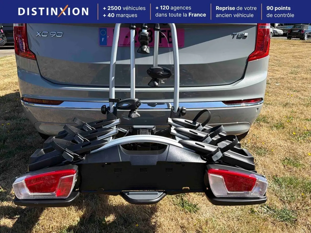 Vue arrière d'un Volvo XC90 gris avec porte-vélos fixé à l'attelage, sur un terrain herbeux.