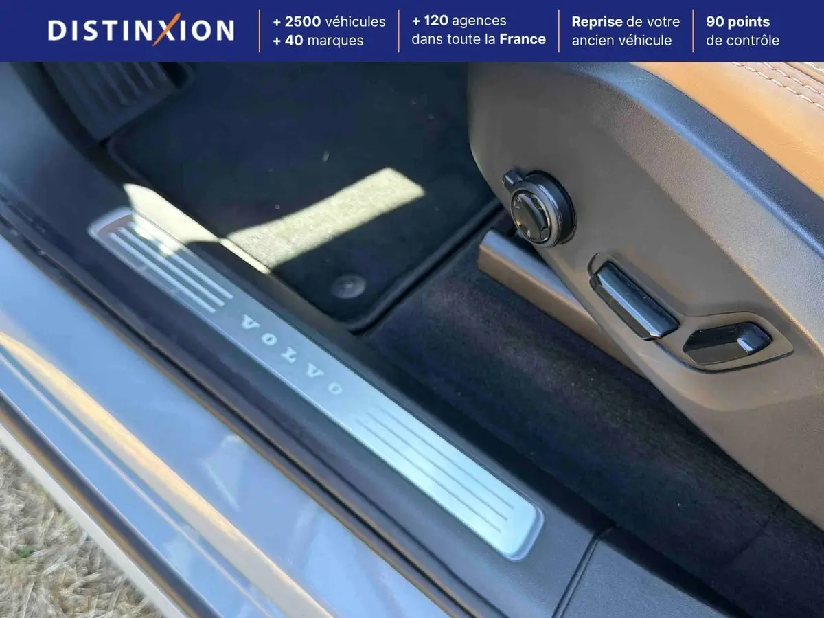 Détail du seuil de porte côté conducteur gris avec inscription Volvo et commandes électriques du siège cuir beige.