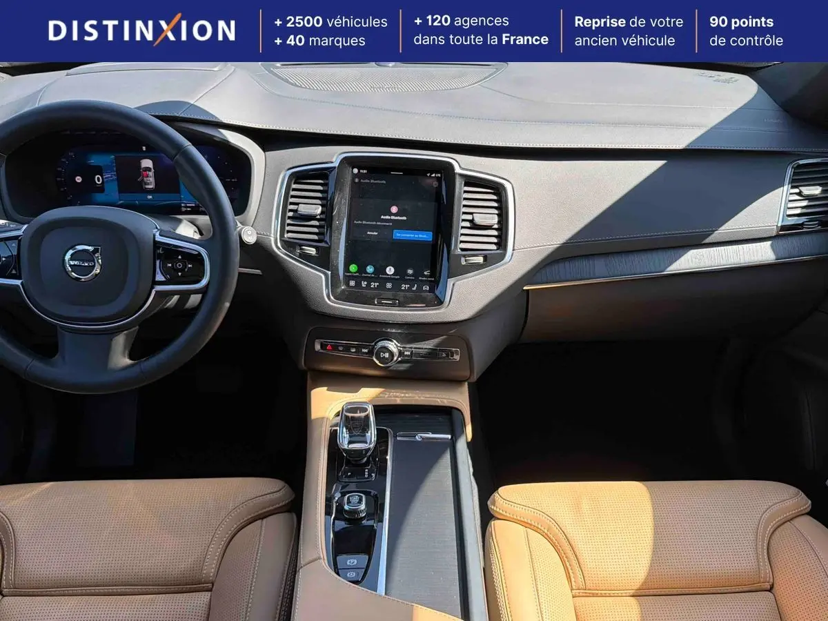Vue intérieure avant du Volvo XC90 2024 avec tableau de bord gris et sellerie cuir beige perforé.