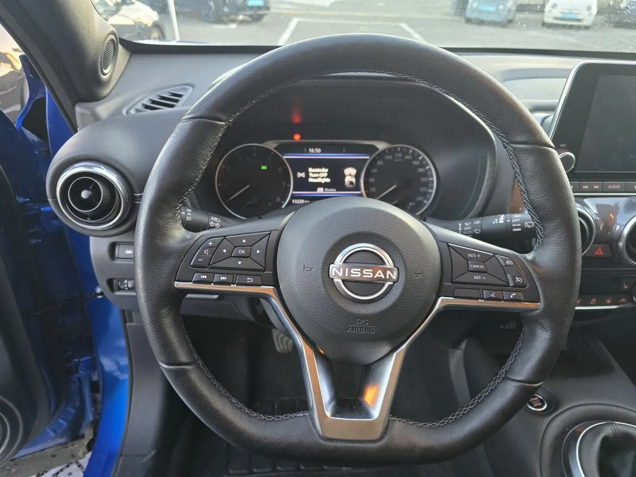 Vue intérieure centrée sur le volant cuir noir du Nissan Juke II bleu magnetic avec tableau de bord digital visible.
