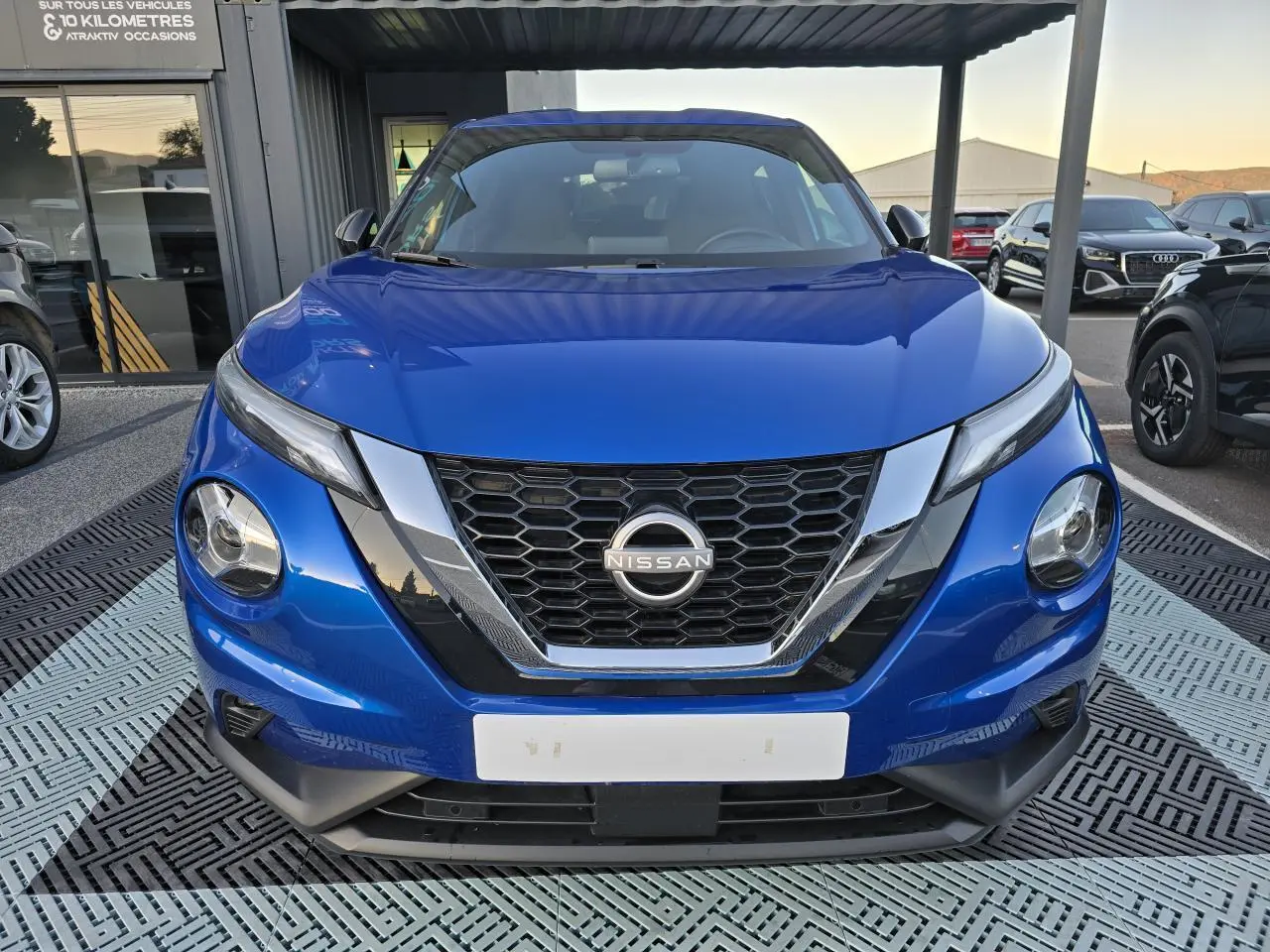 Vue frontale d'un Nissan Juke II bleu magnetic avec calandre en V chromée et phares LED distinctifs.