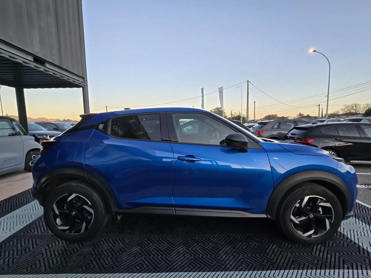 Profil côté gauche du Nissan Juke II bleu magnetic avec jantes alliage noires et toit noir visible en extérieur.