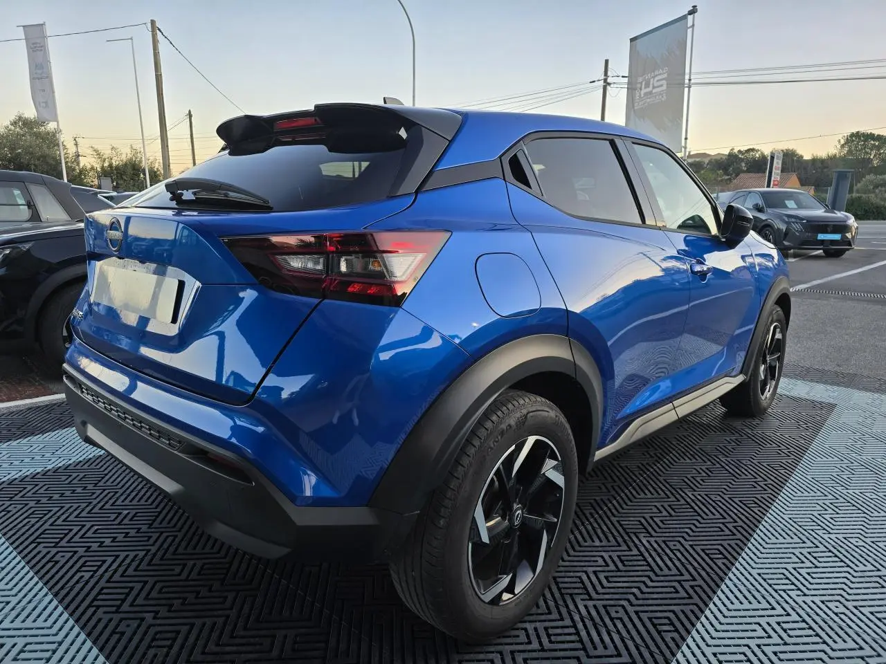 Vue 3/4 arrière droite d'un Nissan Juke II bleu magnetic avec jantes alliage noires et toit noir.