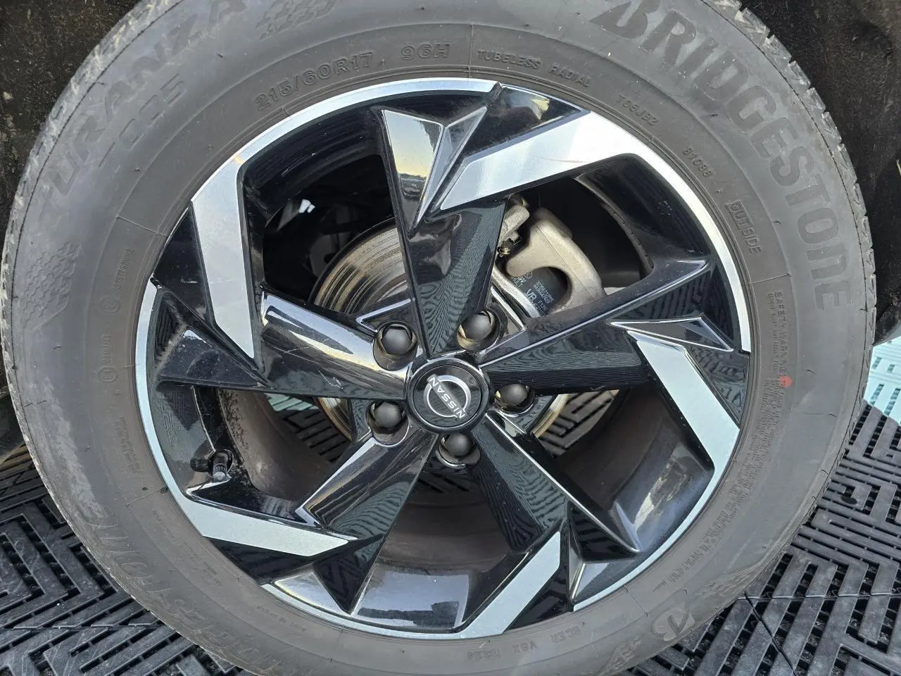 Gros plan sur la jante alliage 17 pouces noire et argentée du Nissan Juke II bleu Magnetic avec logo central Nissan.