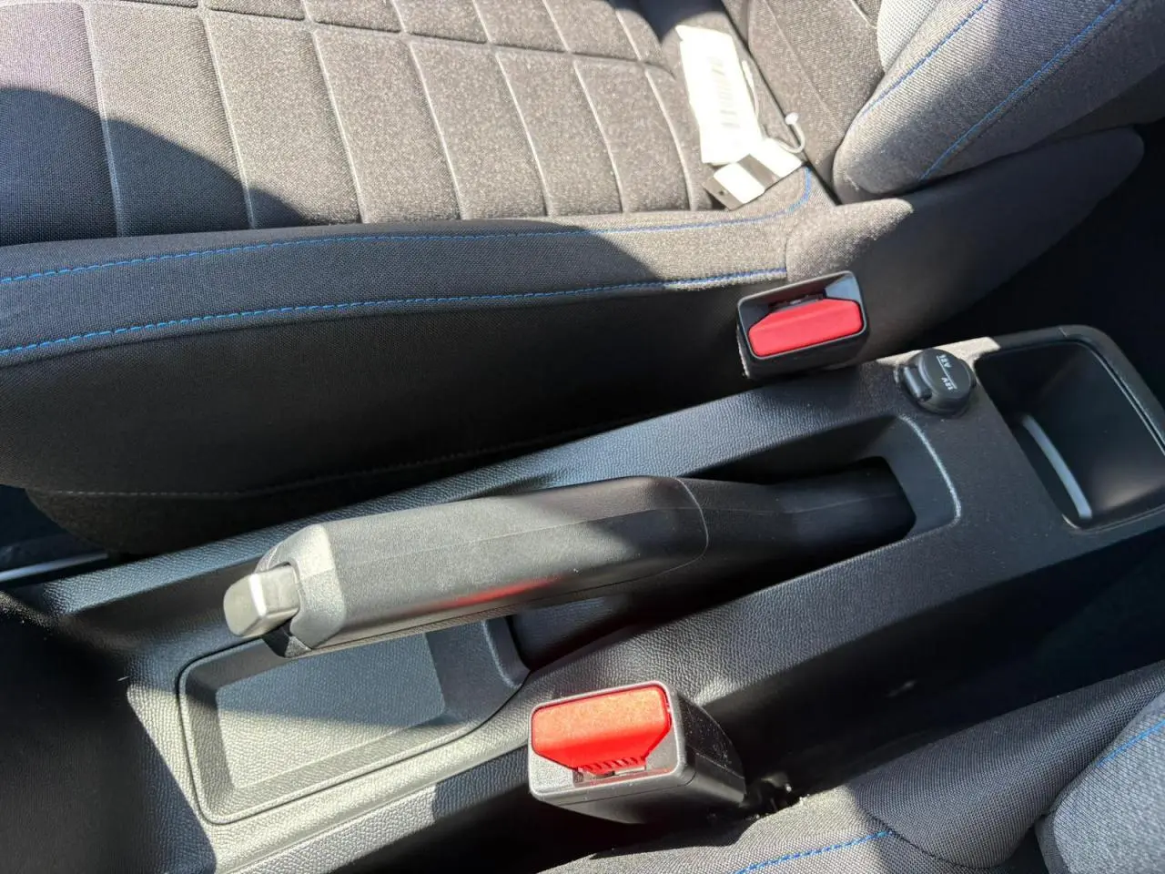 Gros plan sur le frein à main manuel et les ceintures de sécurité rouges entre les sièges avant gris à surpiqûres bleues d'une Citroën C3 2025.