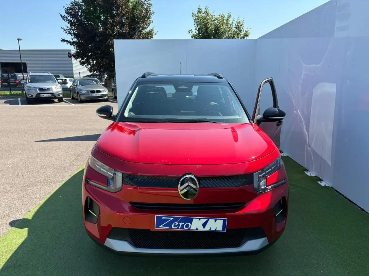Citroën C3 IV rouge Elixir avec toit noir, vue de face, porte avant droite ouverte sur parking.