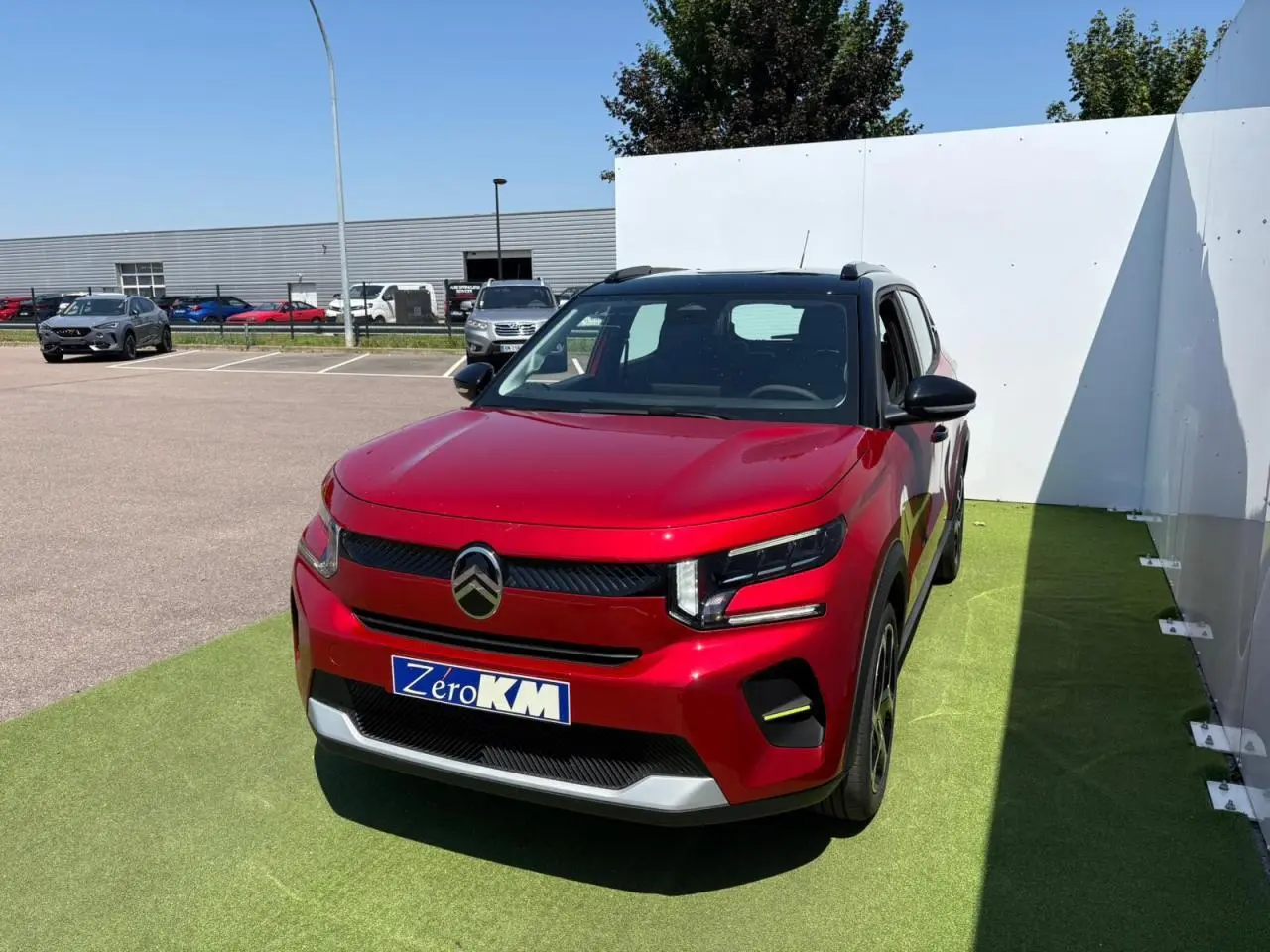 Citroën C3 2025 rouge Elixir avec toit noir, vue 3/4 avant sur parking, plaque Zéro KM visible.