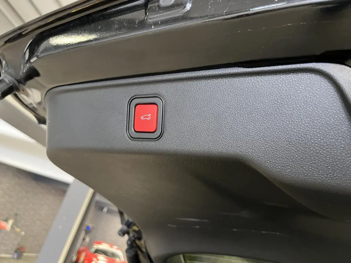 Bouton rouge d'ouverture électrique du hayon sur la partie intérieure du coffre d'une FIAT 600 noire 2024.