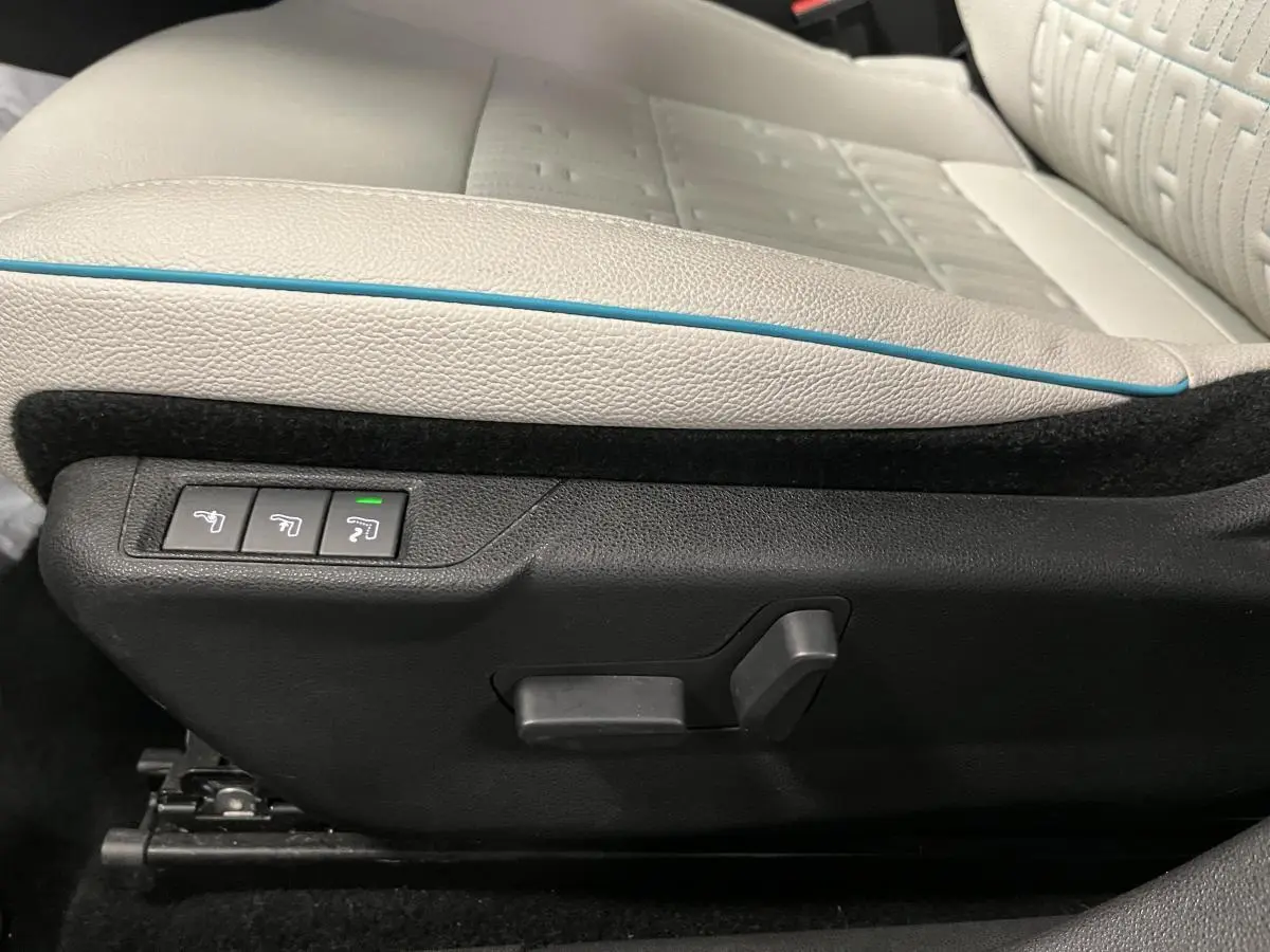 Gros plan sur les commandes électriques du siège conducteur ivoire avec surpiqûre bleue d'une Fiat 600 La Prima noire.