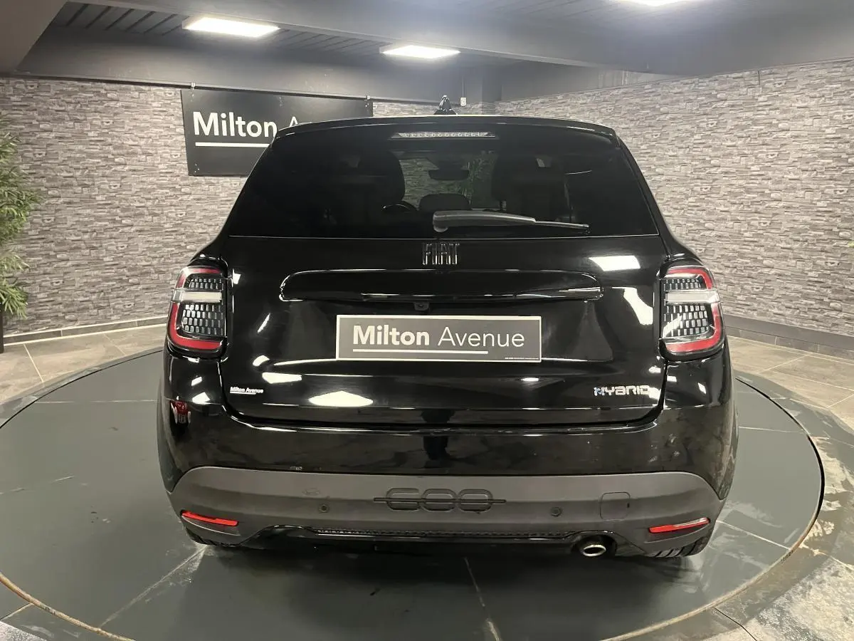 Vue arrière d'une FIAT 600 noire hybride 2024 avec logo chromé et canule d'échappement visible en intérieur showroom.