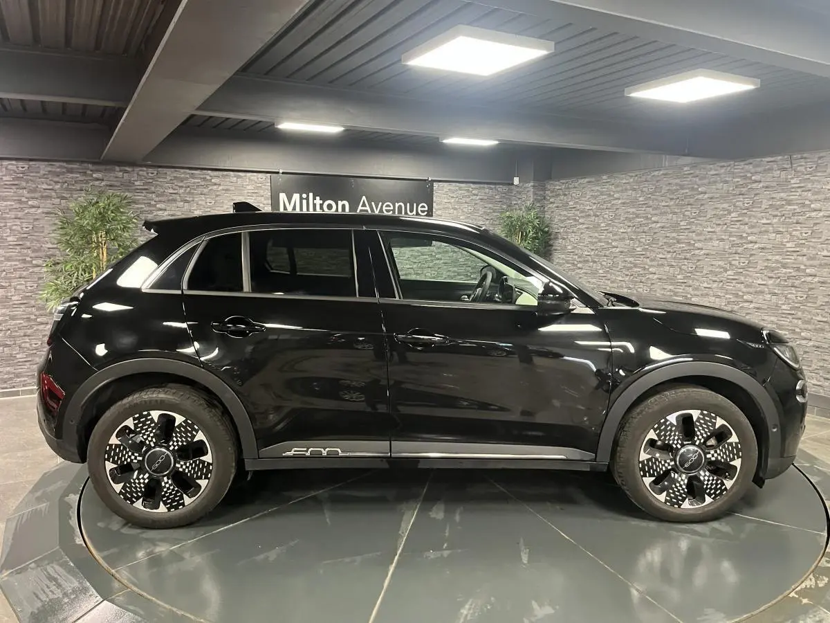 Profil côté gauche d'un FIAT 600 1.2 Hybrid noir brillant avec jantes alliage 18'' diamantées dans un showroom.