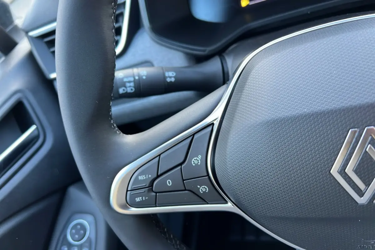 Gros plan sur le volant noir de la Renault Clio 2025 avec commandes intégrées et logo chromé au centre.