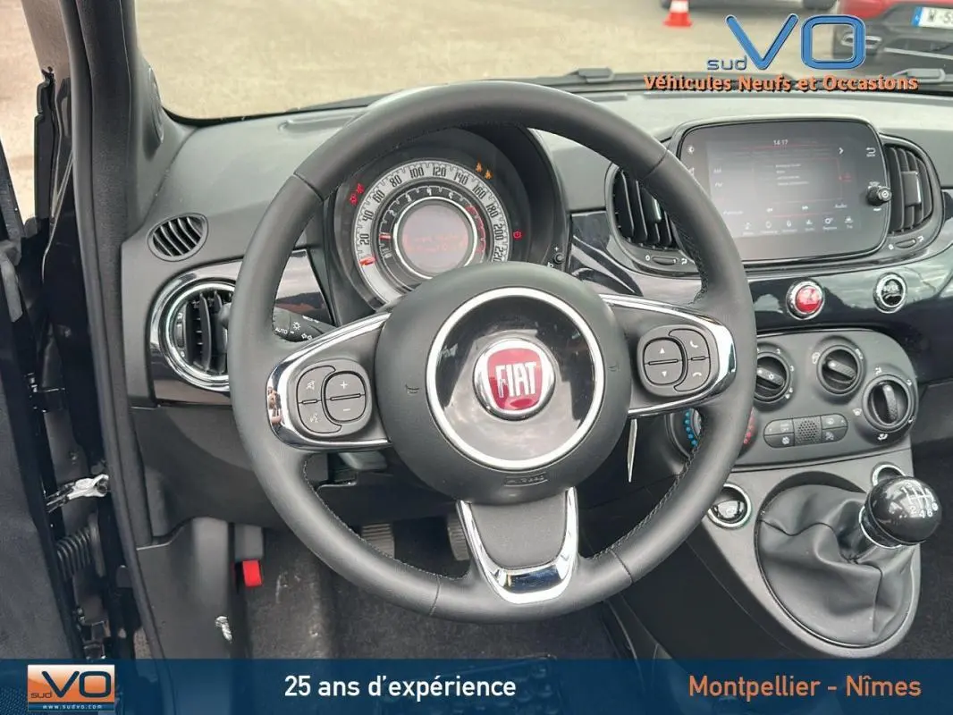 Vue intérieure centrée sur le volant et le tableau de bord noir de la FIAT 500C 2024 avec boîte manuelle et écran tactile.