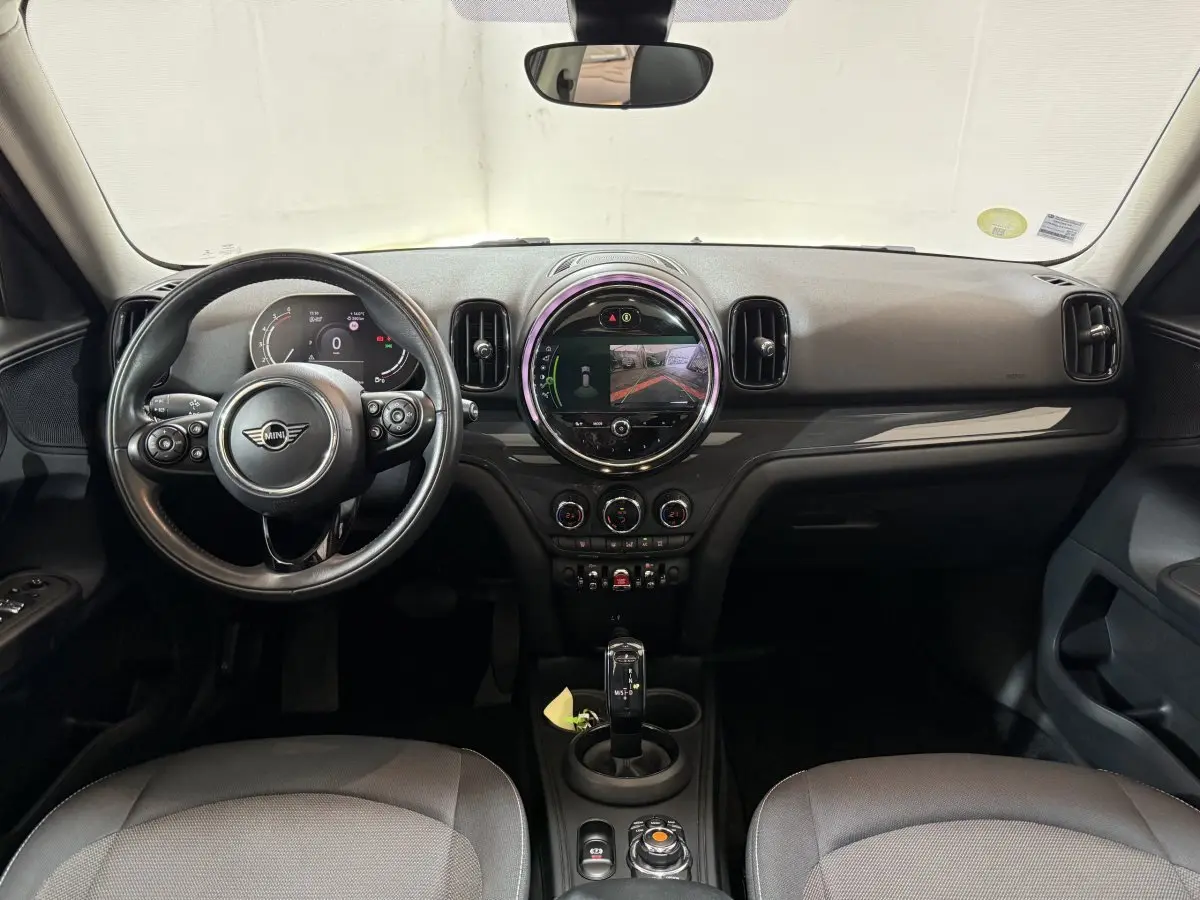 Vue frontale de l'intérieur noir du MINI Countryman 2020 avec volant cuir, écran tactile central rond et levier de vitesse automatique.