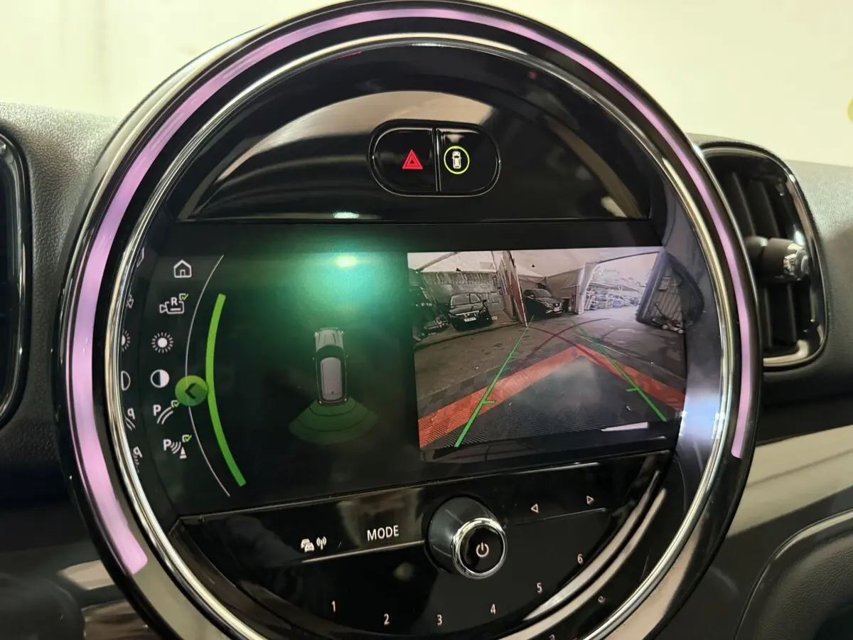 Gros plan sur l'écran tactile rond du tableau de bord du MINI Countryman noir, affichant la caméra de recul et l'aide au stationnement.