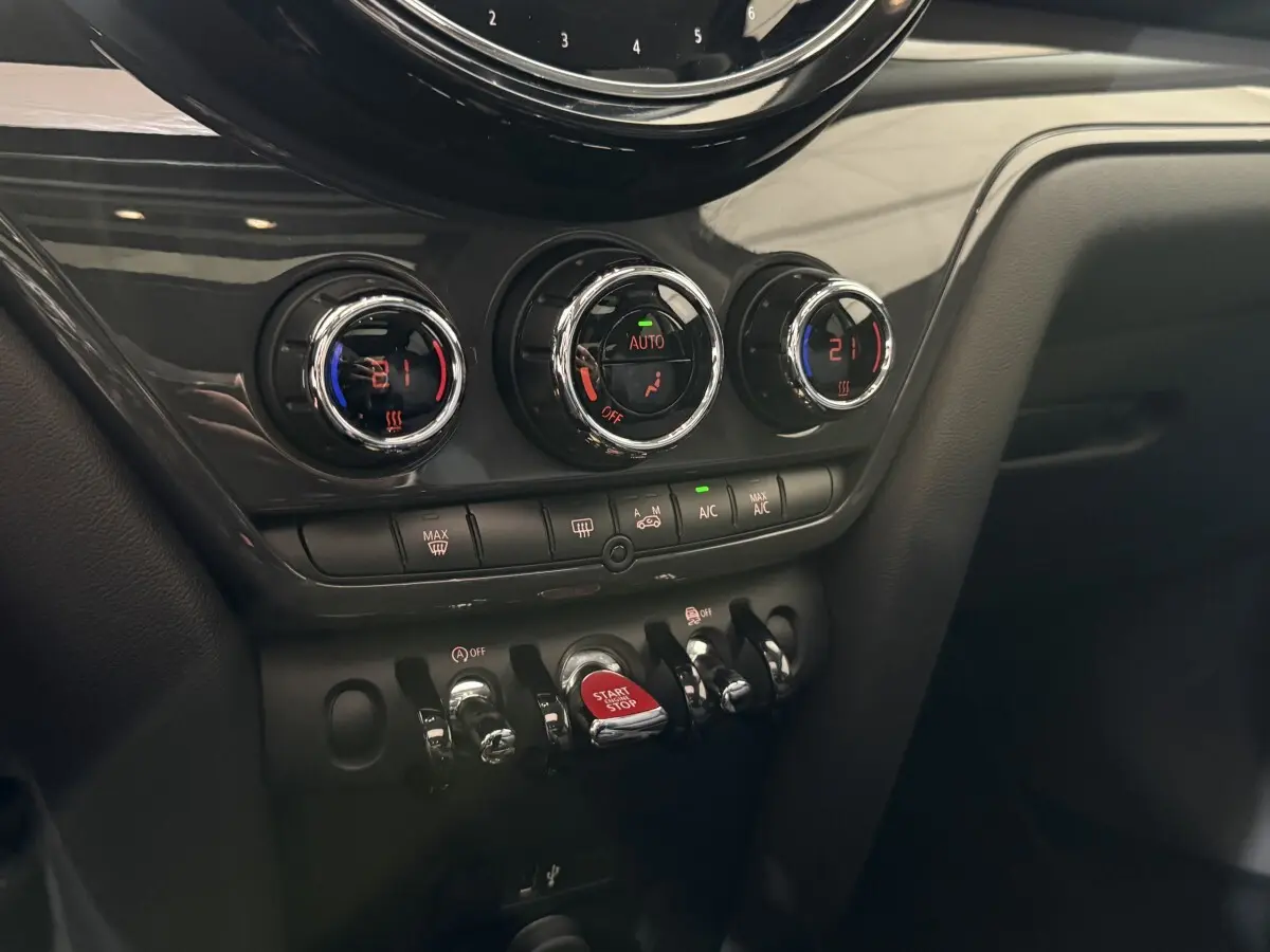 Vue rapprochée du tableau de bord noir de la MINI Countryman 2020, montrant les commandes de climatisation et le bouton start/stop rouge.