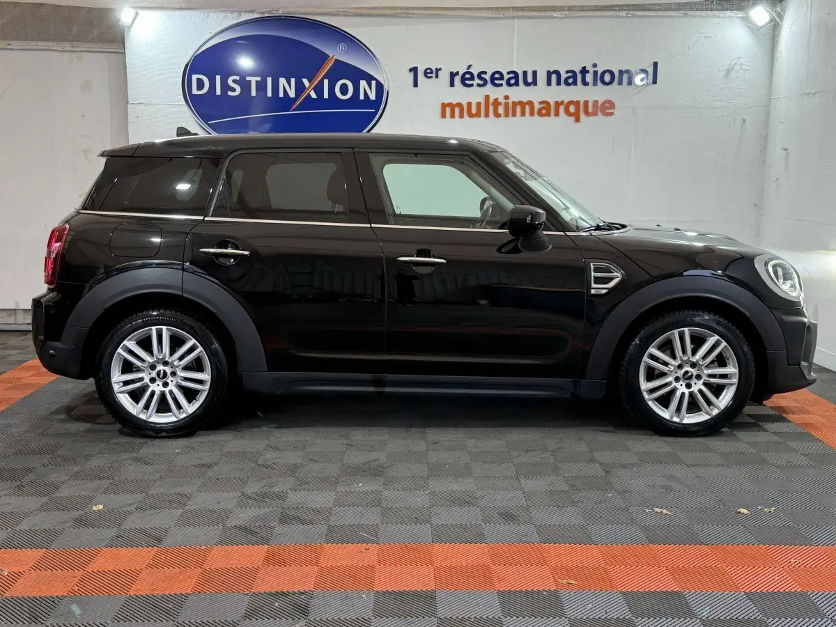 Profil côté gauche d'une MINI Countryman noire 2020, avec jantes alliage et toit noir dans un showroom.