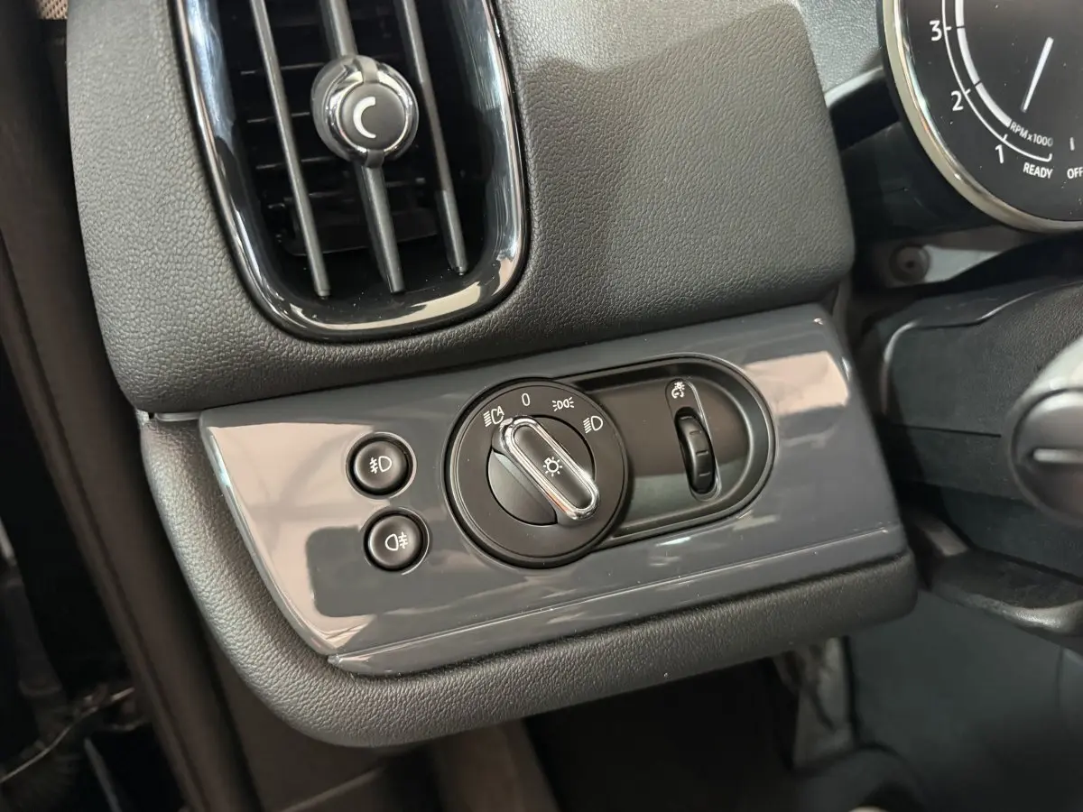 Gros plan sur les commandes d'éclairage gris brillant à gauche du volant dans l'habitacle noir du MINI COUNTRYMAN 2020.