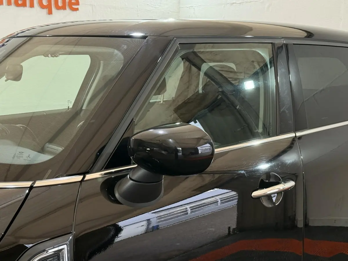 Vue rapprochée du côté gauche d'une MINI Countryman noire 2020, mettant en valeur la portière et le rétroviseur noir brillant.