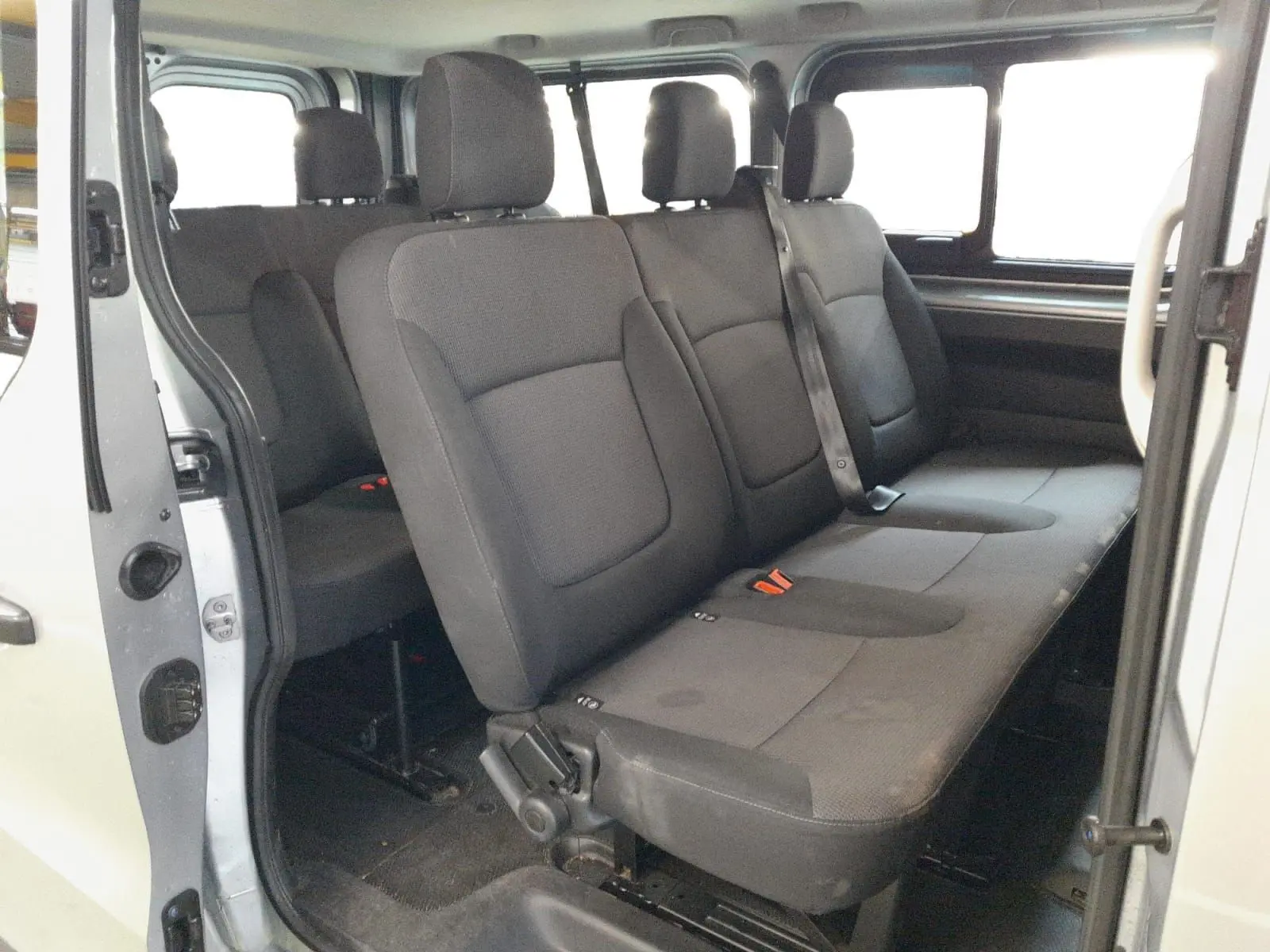 Vue intérieure côté droit des sièges passagers noirs du Renault Trafic Combi gris Highland avec porte coulissante ouverte.