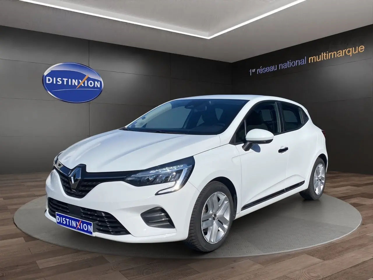 Renault Clio V E-Tech blanche vue 3/4 avant droit, avec phares LED et jantes alliage en showroom.