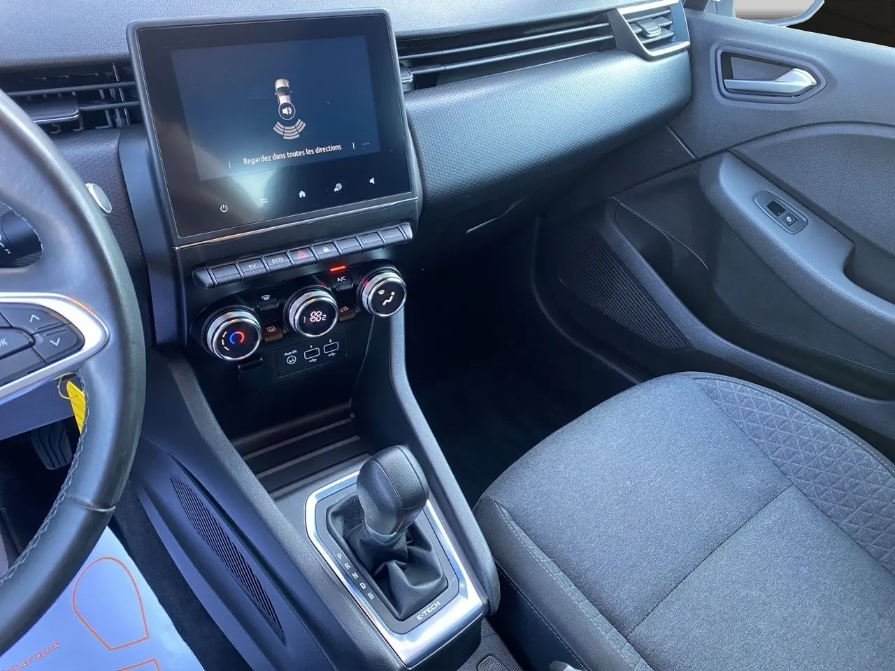 Intérieur de Renault Clio V E-Tech blanc, vue côté passager sur console centrale avec écran tactile et levier de boîte auto.