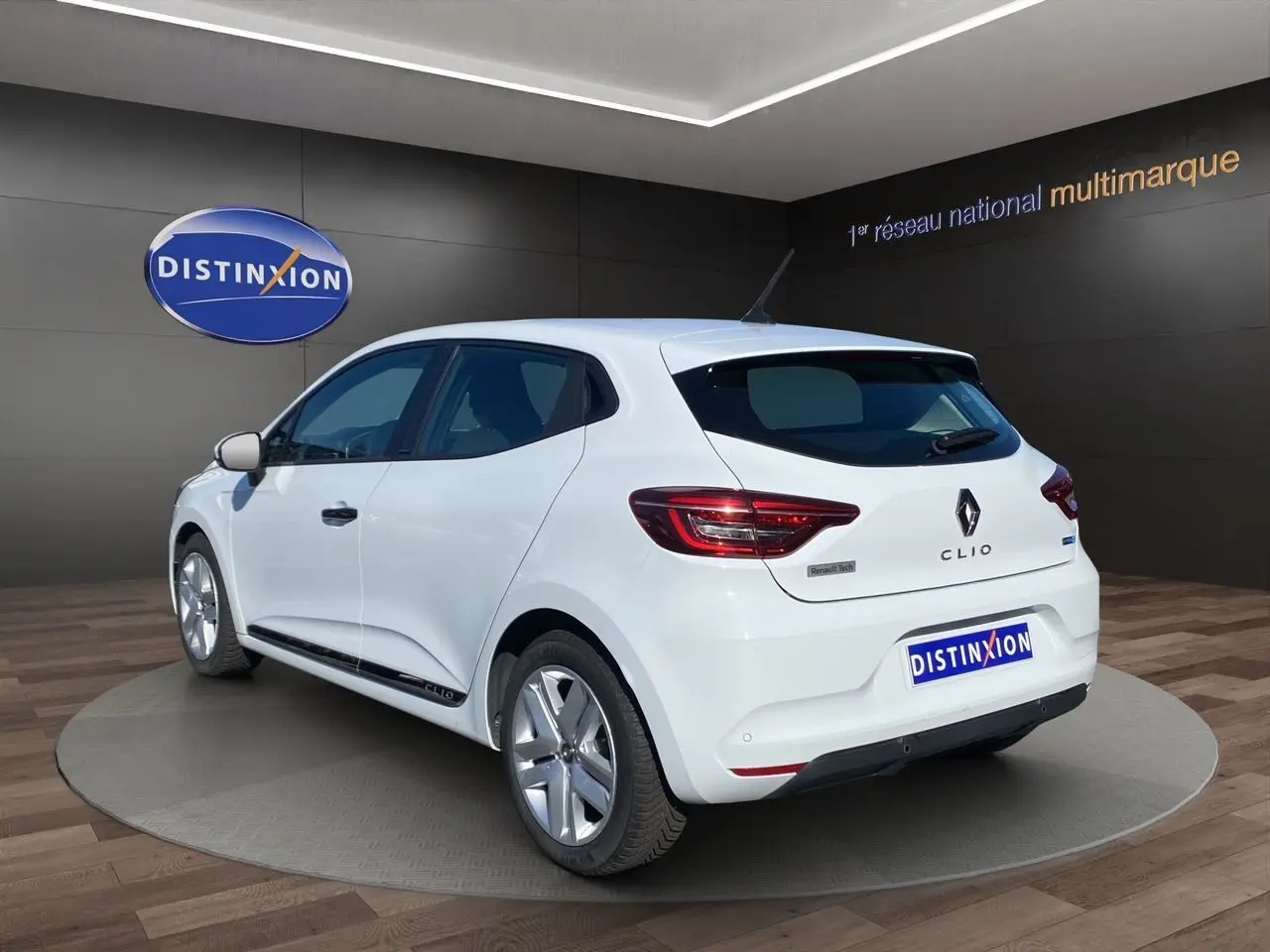Vue 3/4 arrière droite d'une Renault Clio V blanche hybride avec logo Renault et feux arrière LED visibles.