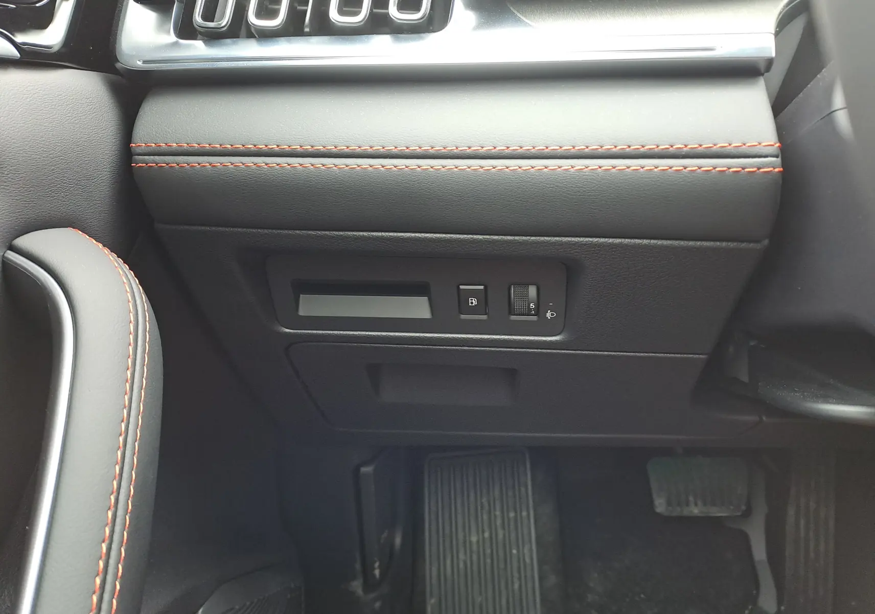 Détail intérieur côté gauche du tableau de bord noir avec surpiqûres rouges et commandes près des pédales du BYD SEAL U 2025.