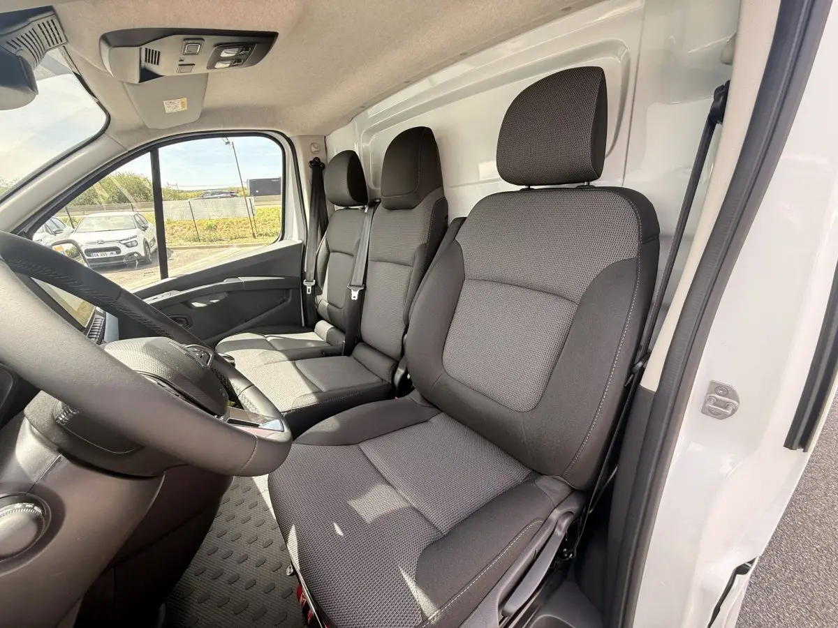 Vue intérieure côté conducteur du Renault Trafic Fourgon blanc 2025, montrant les sièges avant en tissu gris.