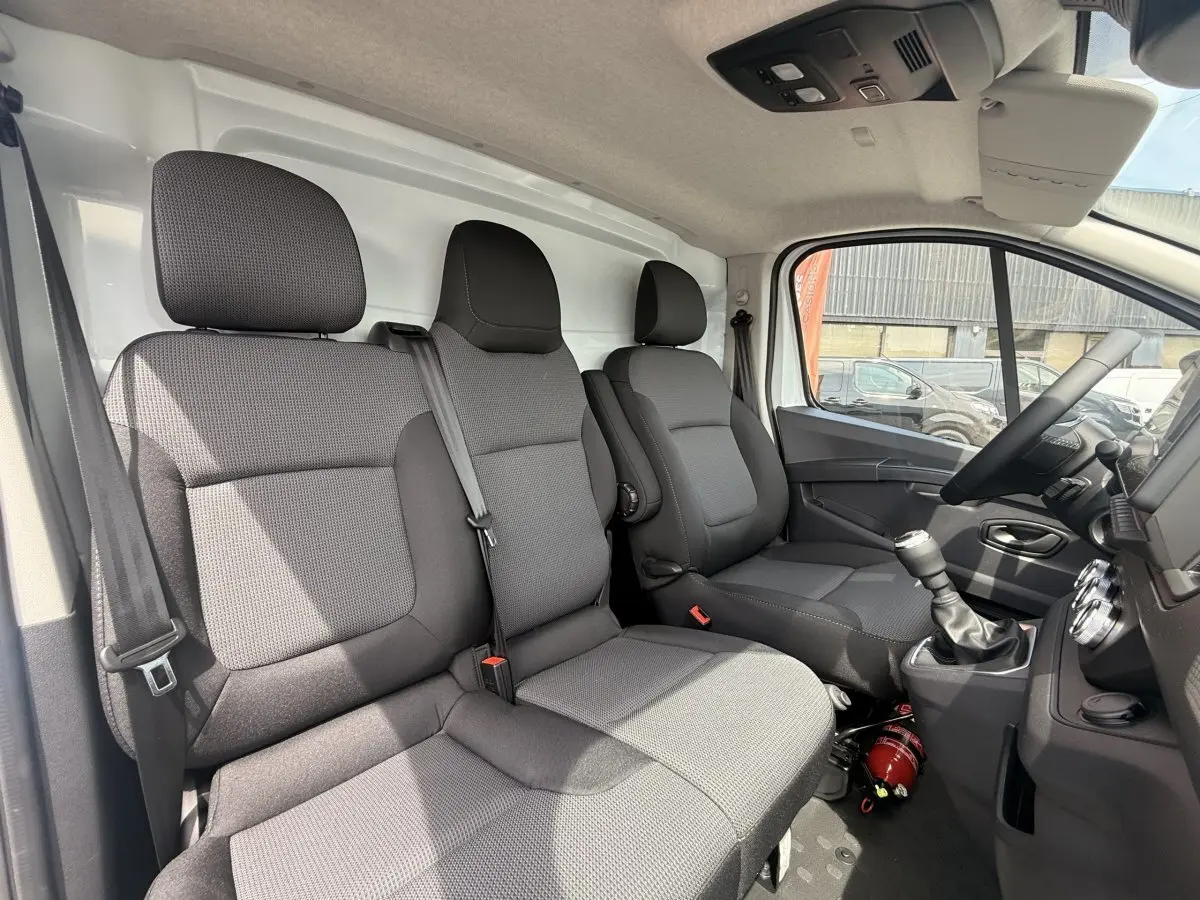 Vue intérieure côté conducteur du Renault Trafic Fourgon 2025 avec sièges tissu gris et tableau de bord noir.