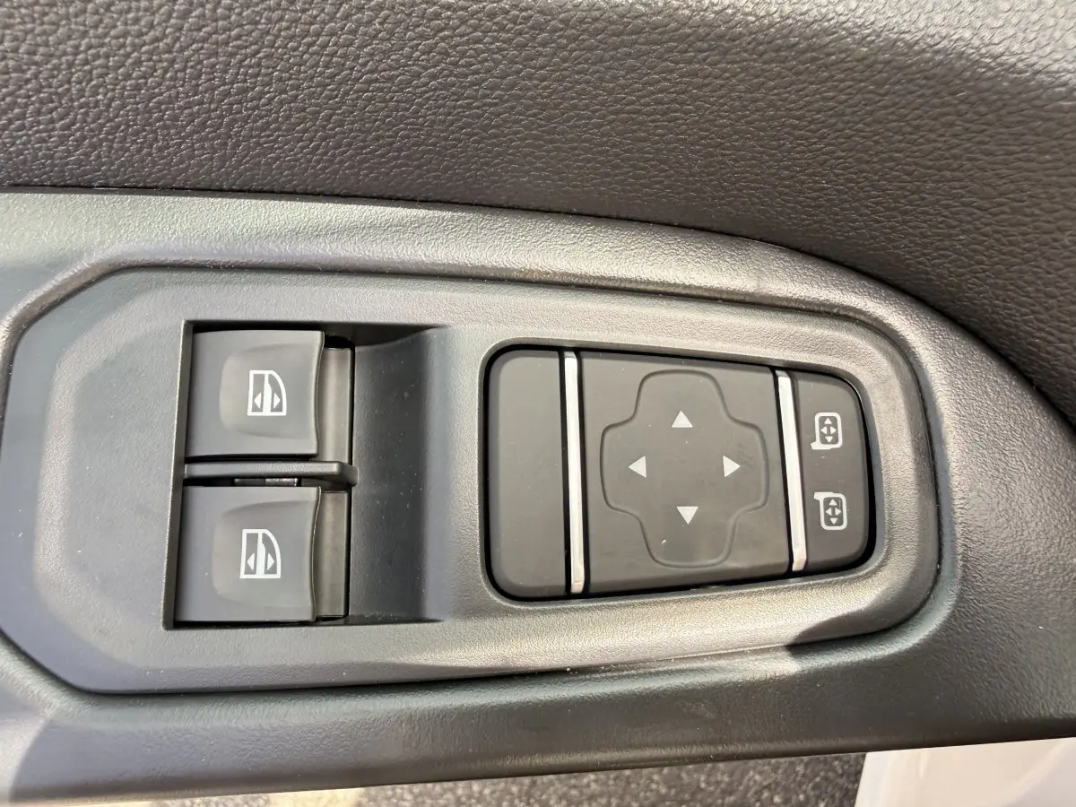 Gros plan sur les commandes électriques des vitres et rétroviseurs côté conducteur du Renault Trafic Fourgon blanc.